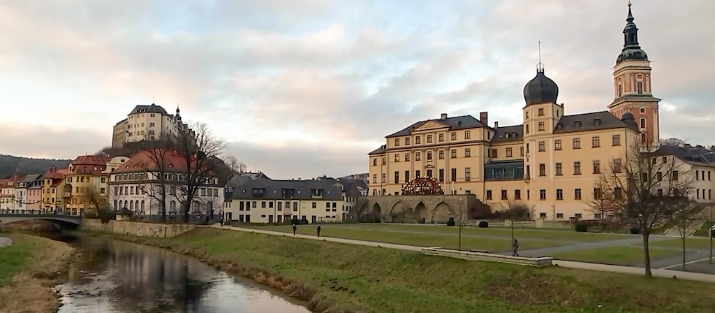 Ein Schloss im Winter, davor eine große Grünfläche und ein Fluss.