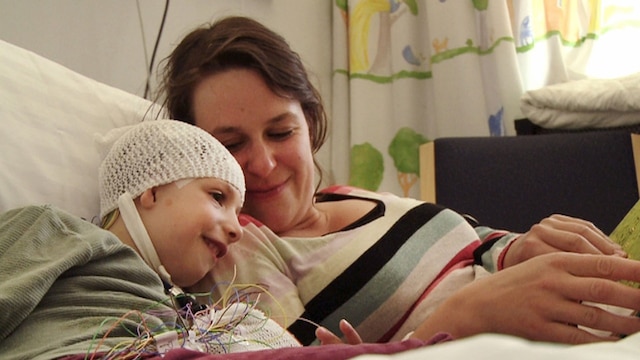 Eine Frau liegt mit ihrem Kind in einem Krankenhaus-Bett.